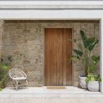 Close-up of entrance to modern Buenos Aires home with chair and potted plants on porch either side of front door.